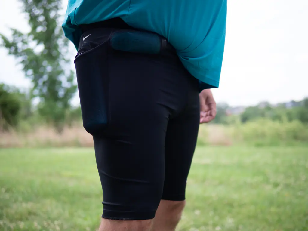 A runner wearing the half tights, with a 500ml soft flask in the side pocket and a 150ml nutrition flask in the front right waist pocket, shown from a front side angle