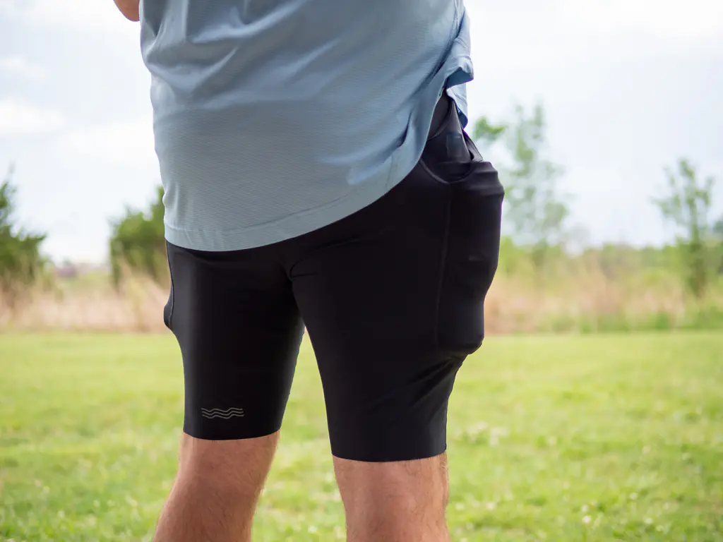 A rear-side-view of a runner wearing the half tights, with the side pockets loaded with both a 500ml soft flask and a 150ml nutrition flask, which bulges quite a bit.