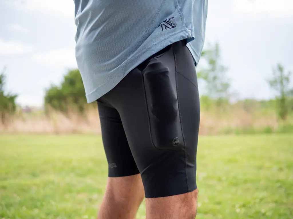 A side-view of a runner wearing the half tights, with the side pockets loaded with both a 500ml soft flask and a 150ml nutrition flask, which bulges quite a bit.