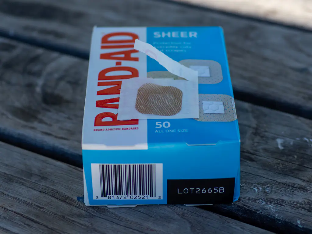 A closeup of the BAND-AID Sheer Spots unwrapped, showing the square, classic BAND-AID colored bandage.